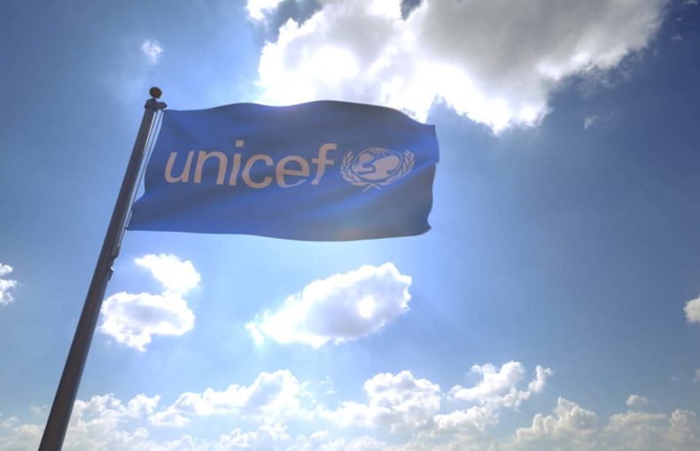 UNICEF Flag waving on a flagpole in front of a blue sky with clouds