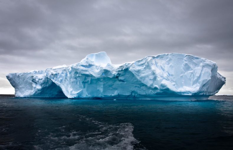 Iceberg floating in ocean with dark sky behind
