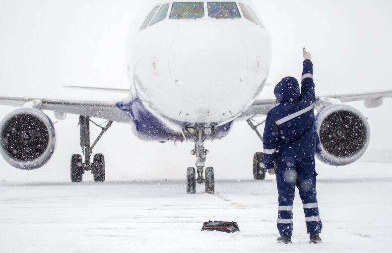 Member of ground crew parks passenger airliner on airport apron in blizzard