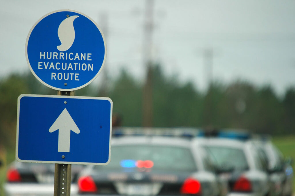 A hurricane evacuation route sign posted along a road with police cars in the background