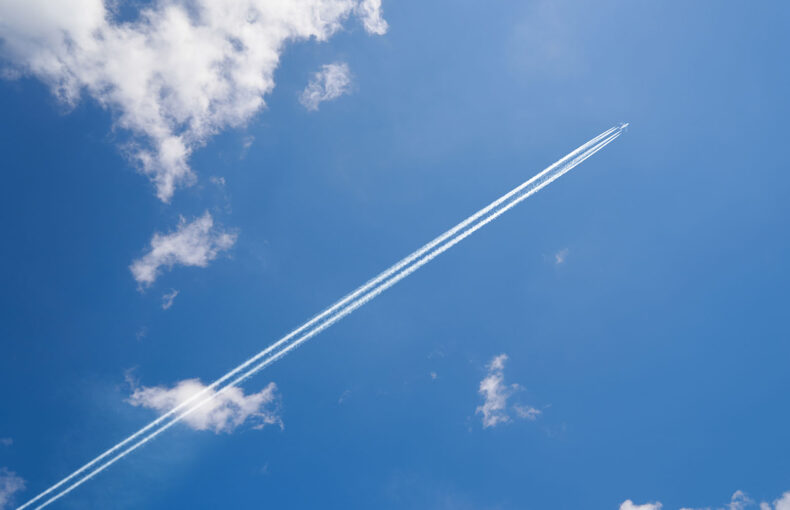 Airplane contrail against blue sky with white clouds