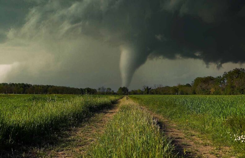 Dirt road through the field with a tornado storm in the background