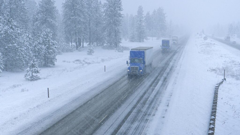 Freight trucks navigate the slippery country road in low visibility during an intense blizzard during La Niña